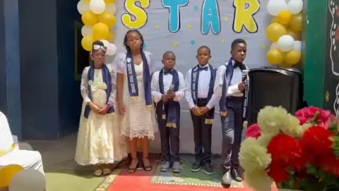 Pupils in sashes standing on stage under the Star banner